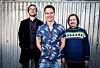 GLAD GUTT: Vegard Mostue Johannessen smiler fra øre til øre etter at lønna hans er gått opp og han har fått etterbetalt manglende lønn. Det kan han takke tillitsvalgte Håvard Lundkvist (t.v) og Anders Oak for.