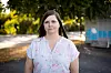 Sarah Henriksen i blomstrete bluse står utendørs foran det brannskadde hjemmet i Krokstadelva.