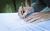 Hender signerer et dokument med penn ved et skrivebord.